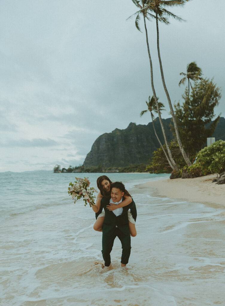 Bride and groom walking barefoot along Kaaawa Beach during golden hour
