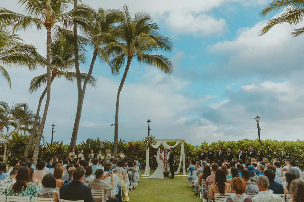 Outdoor wedding ceremony with palm trees and guests seated.

