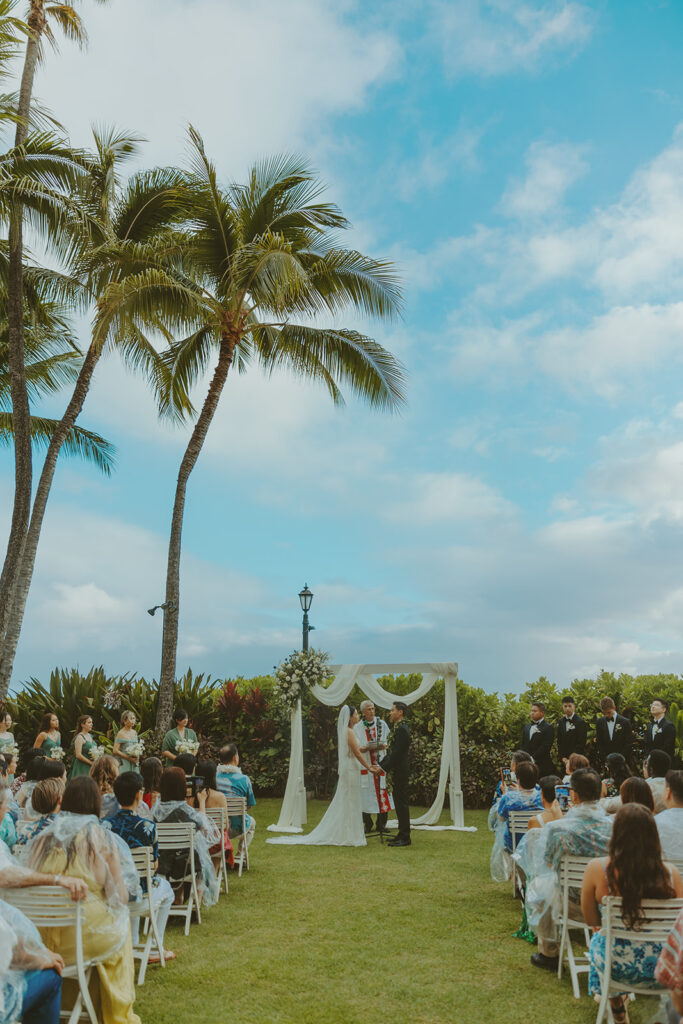 Outdoor wedding ceremony with palm trees and guests seated.
