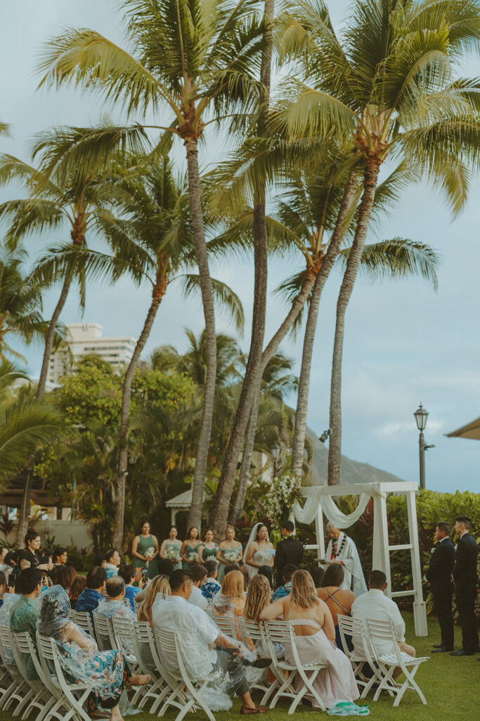 Outdoor wedding ceremony with palm trees and guests seated.