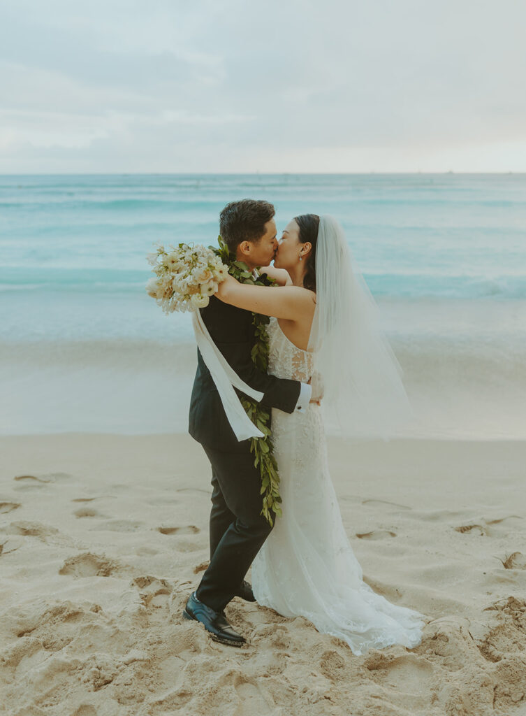 Bride holding a bouquet of white flowers on the beach.
