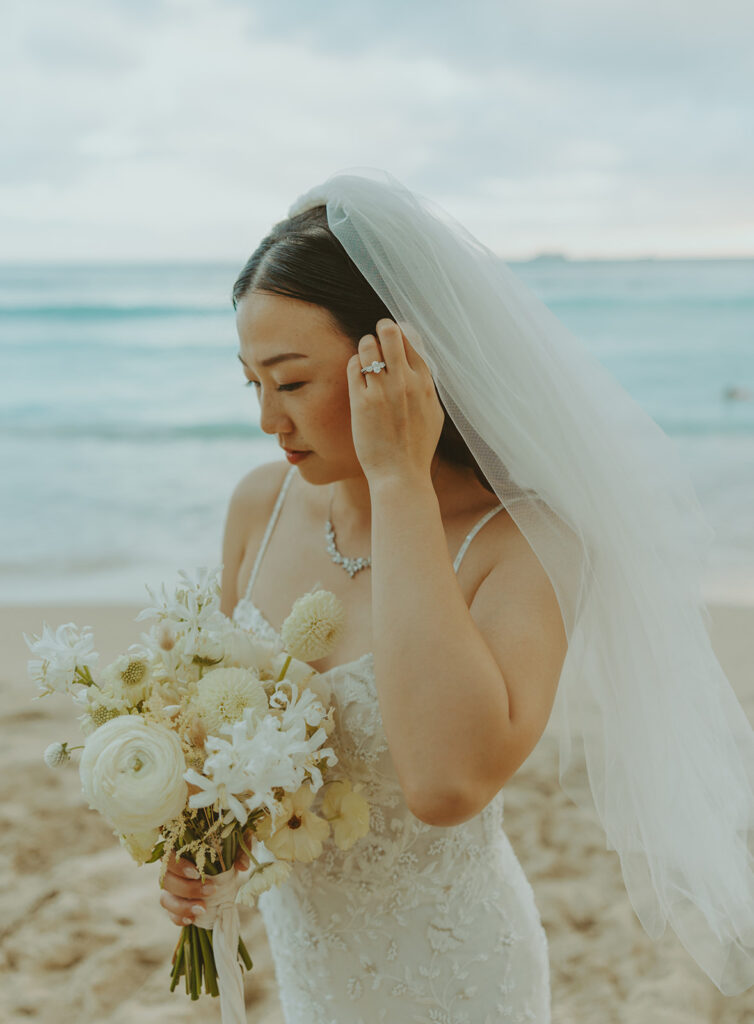 Bride holding a bouquet of white flowers on the beach.
