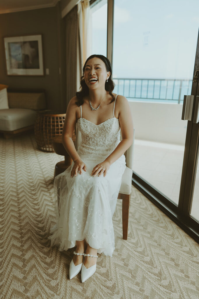 Bride smiling in a lace wedding dress and veil by the window. | Moana Surfrider
