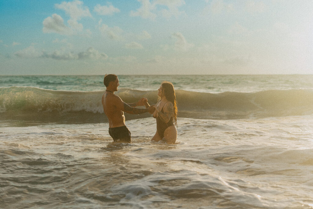 Couple laughing and playing in the ocean during an Oahu couples photoshoot at sunrise
