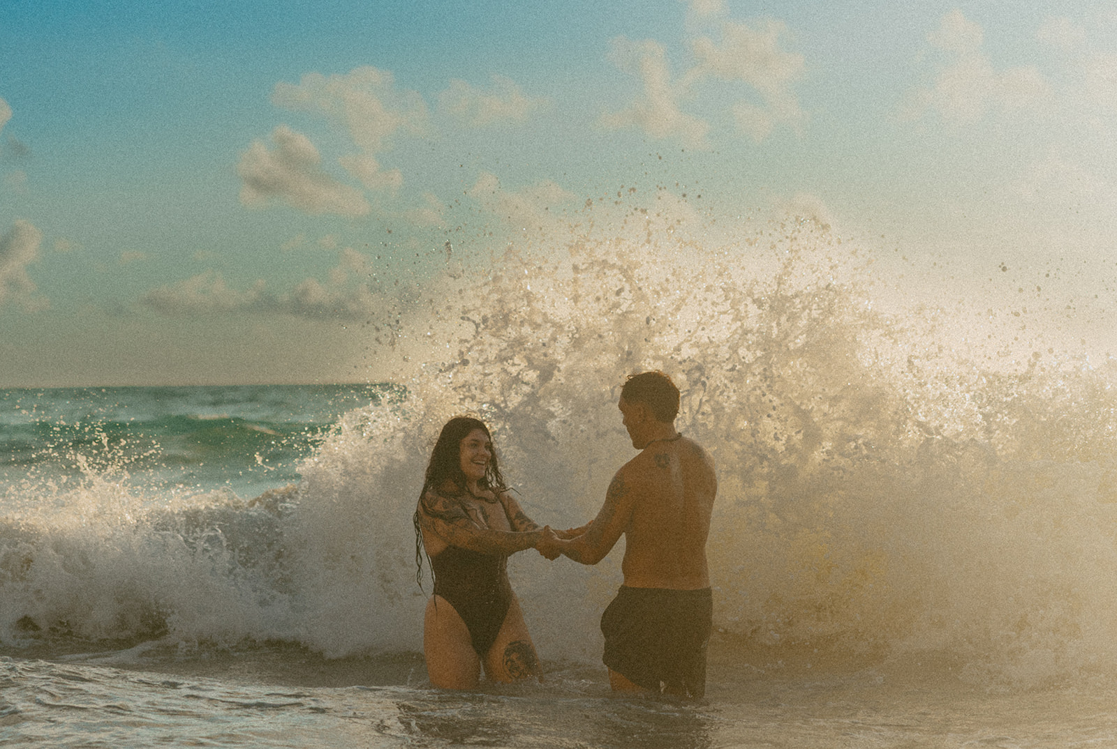 Couple laughing and playing in the ocean during an Oahu couples photoshoot at sunrise