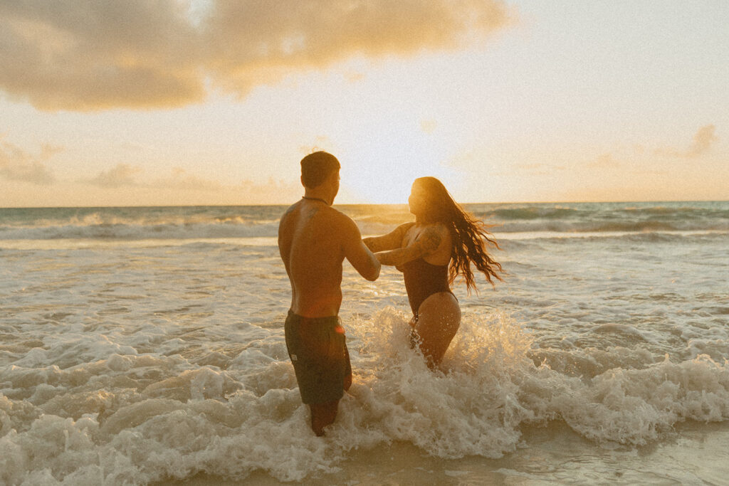 Couple laughing and playing in the ocean during an Oahu couples photoshoot at sunrise
