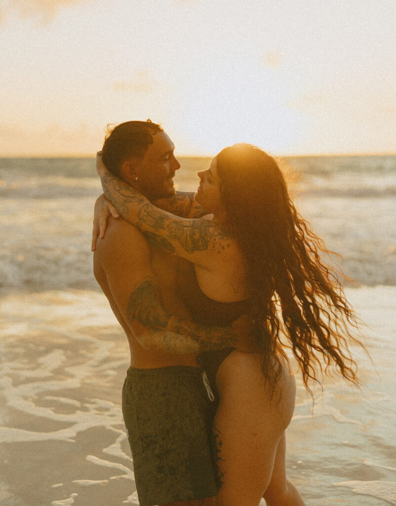 Couple laughing and playing in the ocean during an Oahu couples photoshoot at sunrise
