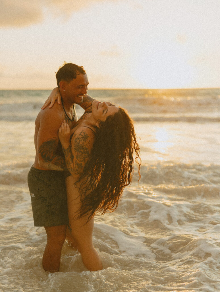 Couple laughing and playing in the ocean during an Oahu couples photoshoot at sunrise
