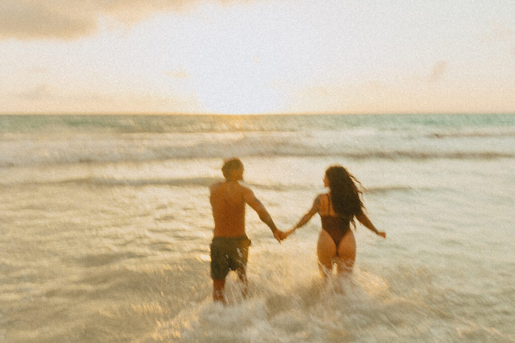 Couple laughing and playing in the ocean during an Oahu couples photoshoot at sunrise
