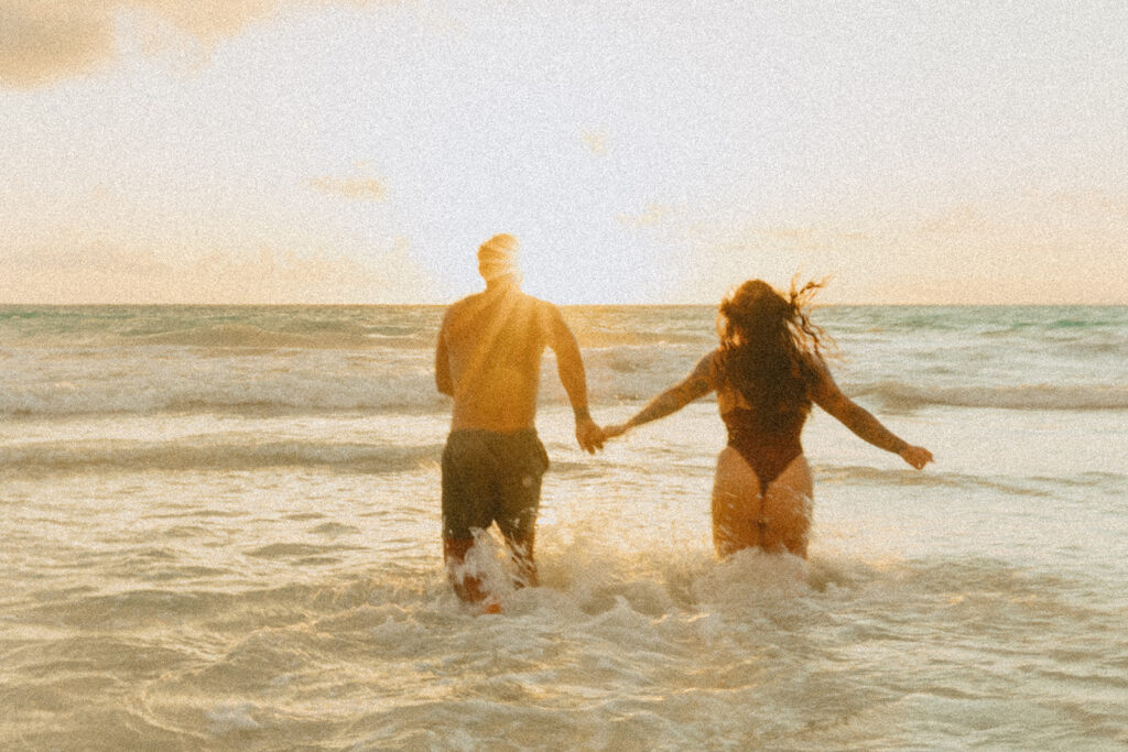 Couple laughing and playing in the ocean during an Oahu couples photoshoot at sunrise
