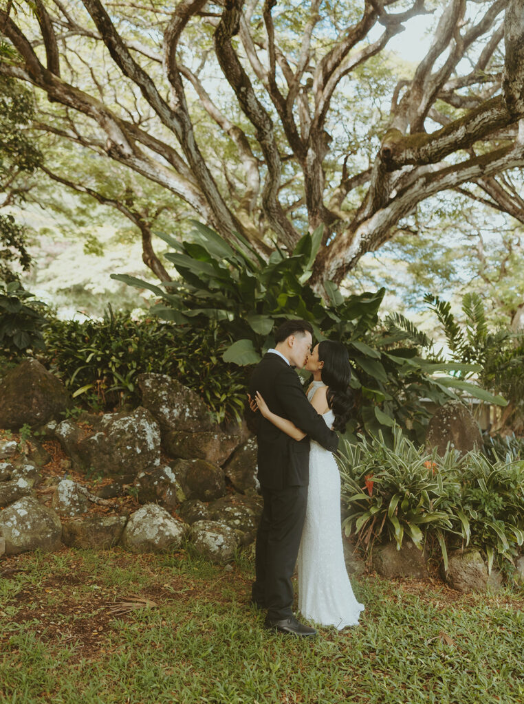 Bride and groom exchanging vows at Kualoa Ranch venue with mountain views in the background.
