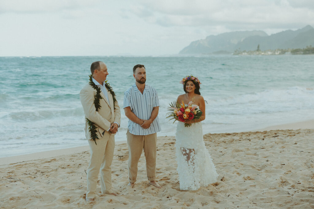 Bride and groom celebrating with their wedding party along the ocean shoreline.