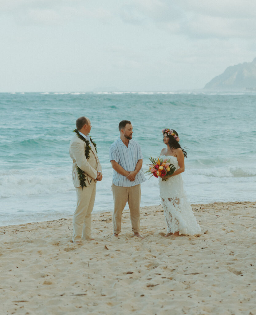 Bride and groom celebrating with their wedding party along the ocean shoreline.

