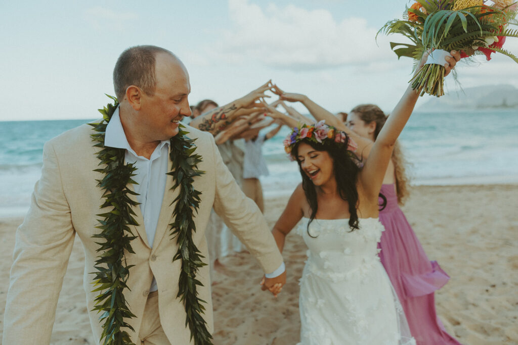 Bride and groom celebrating with their wedding party along the ocean shoreline.