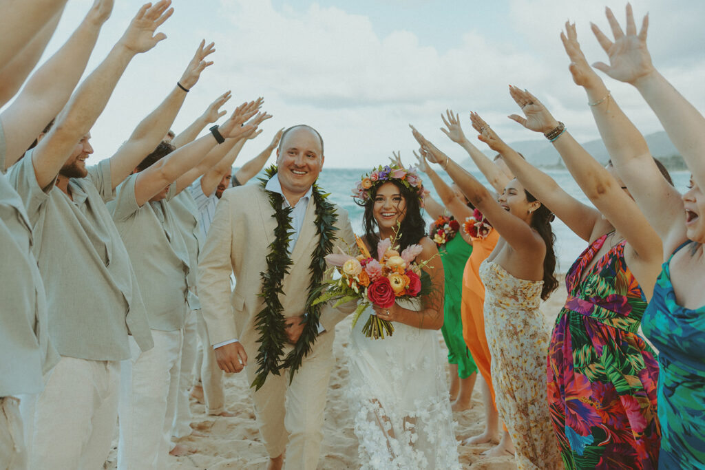 Bride and groom celebrating with their wedding party along the ocean shoreline.
