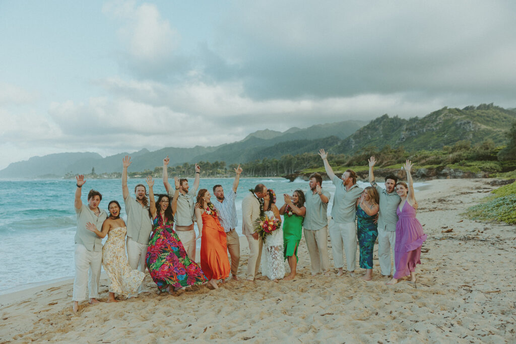 Bride and groom celebrating with their wedding party along the ocean shoreline.

