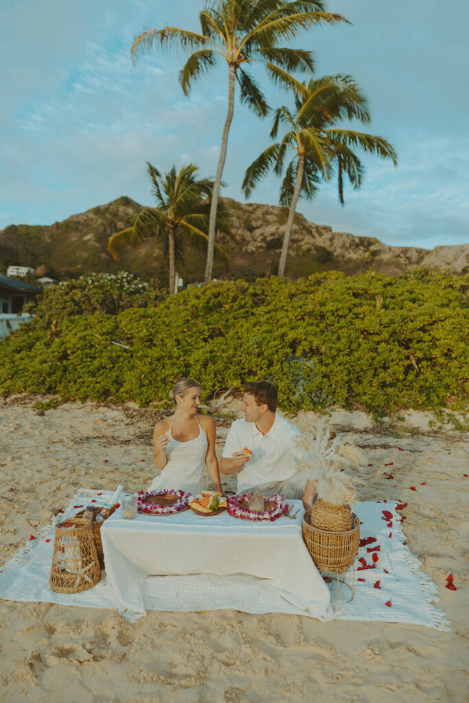 Sunrise light reflecting on a beachside picnic setup with flowers and blankets
