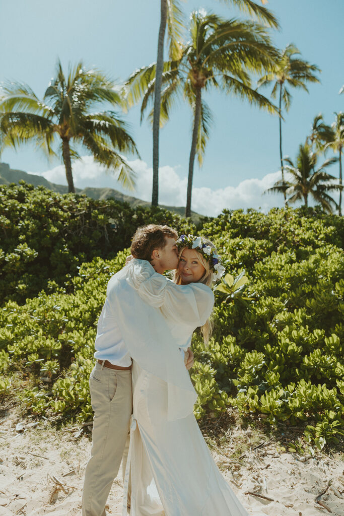 Bride and groom walking through Kualoa Regional Park with mountain views in the background.
