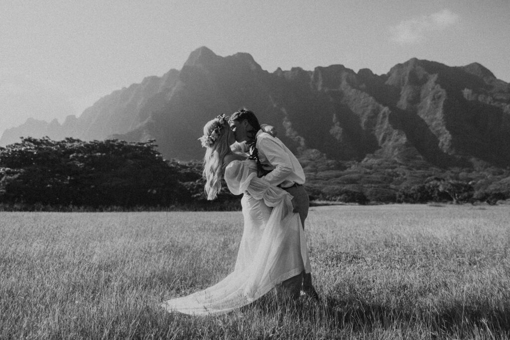 Bride and groom walking through Kualoa Regional Park with mountain views in the background.