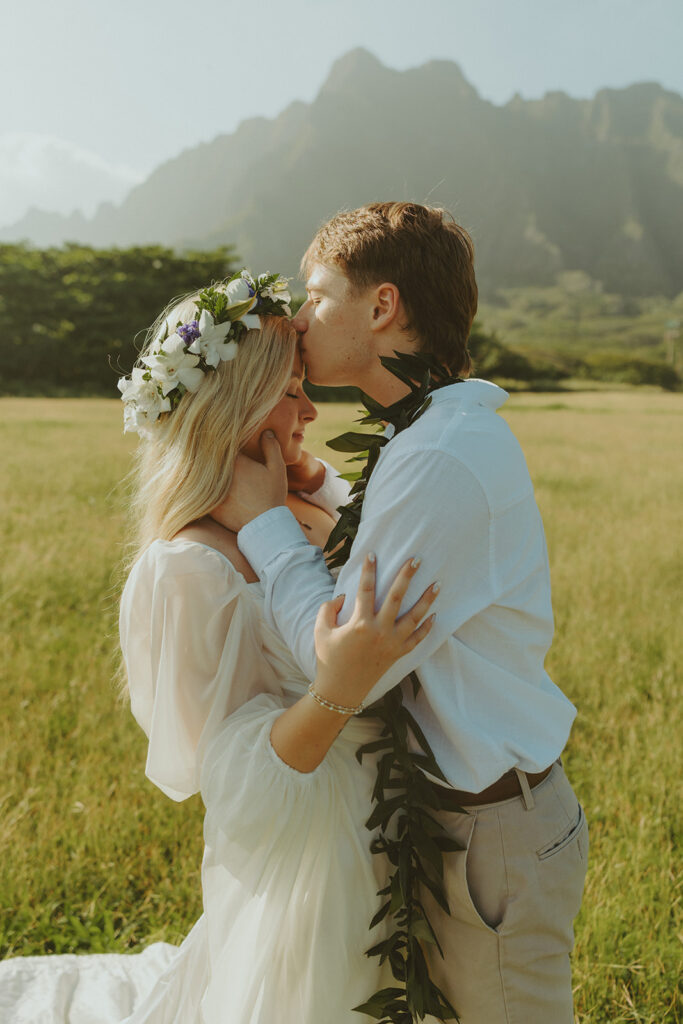 Bride and groom walking through Kualoa Regional Park with mountain views in the background.
