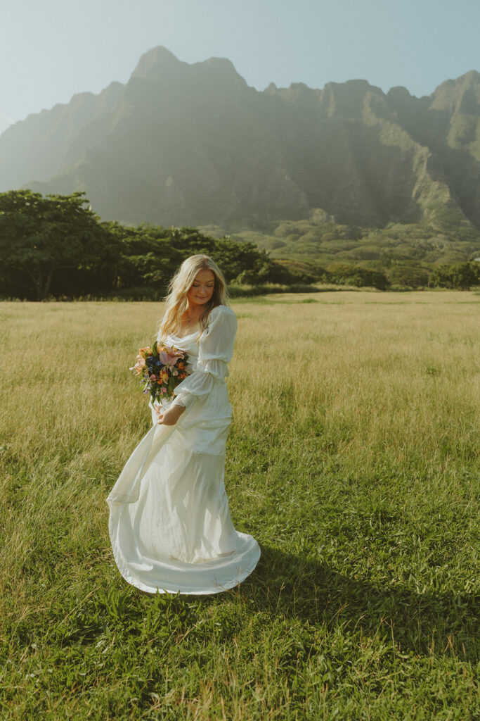 Bride and groom walking through Kualoa Regional Park with mountain views in the background.
