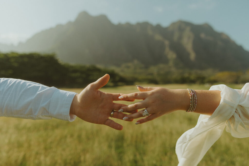 Bride and groom walking through Kualoa Regional Park with mountain views in the background.
