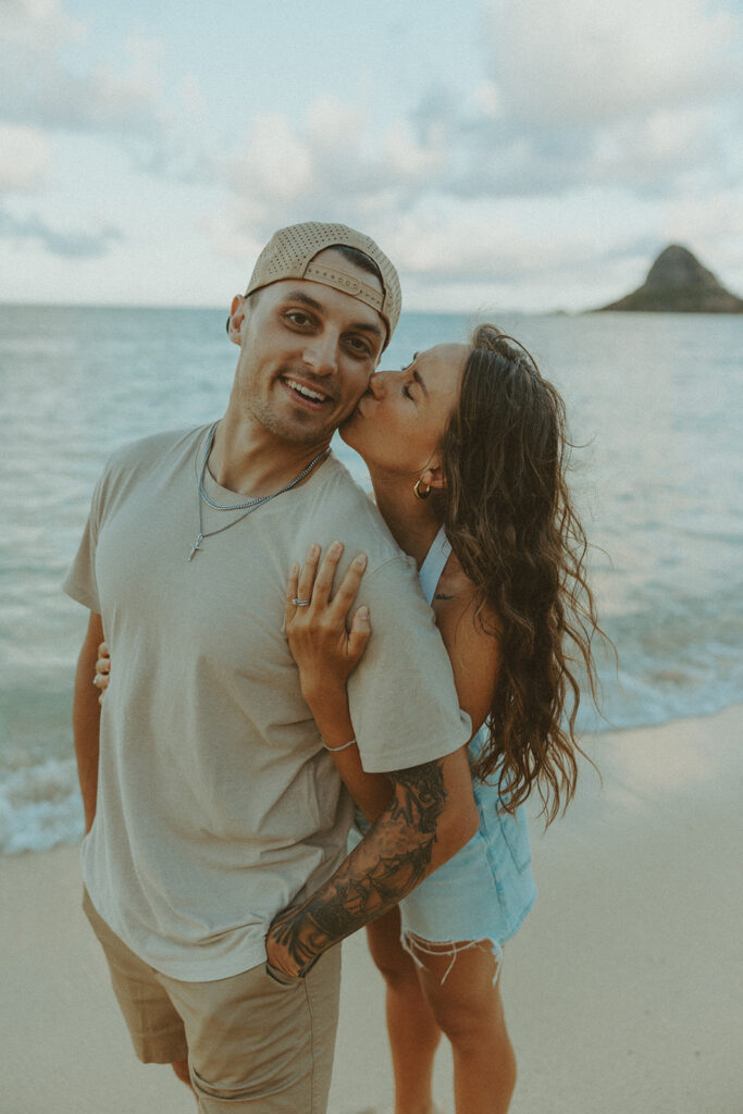 Romantic couple embracing on the beach with Chinaman’s Hat visible behind them
