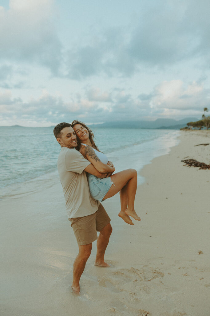 Couple walking along the shoreline at Kualoa Regional Park with ocean and mountain views in the background
