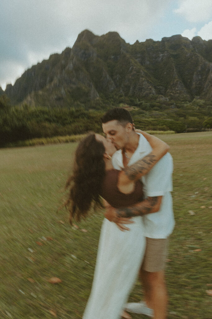 Couple walking along the shoreline at Kualoa Regional Park with ocean and mountain views in the background
