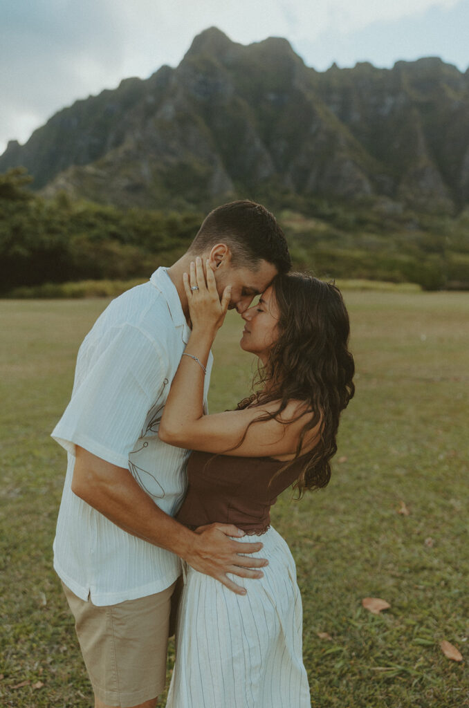 Couple walking along the shoreline at Kualoa Regional Park with ocean and mountain views in the background
