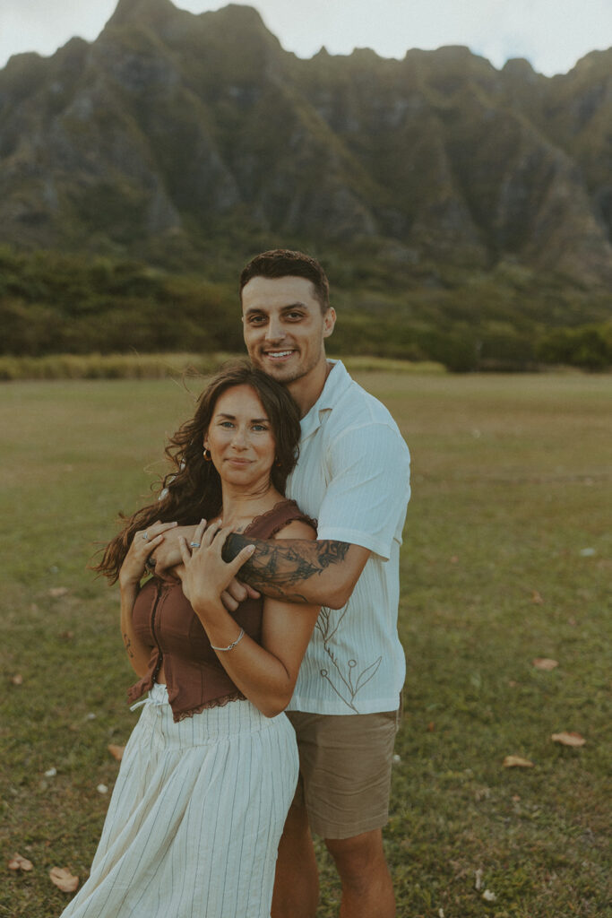 Couple walking along the shoreline at Kualoa Regional Park with ocean and mountain views in the background
