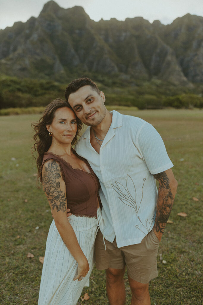 Couple walking along the shoreline at Kualoa Regional Park with ocean and mountain views in the background
