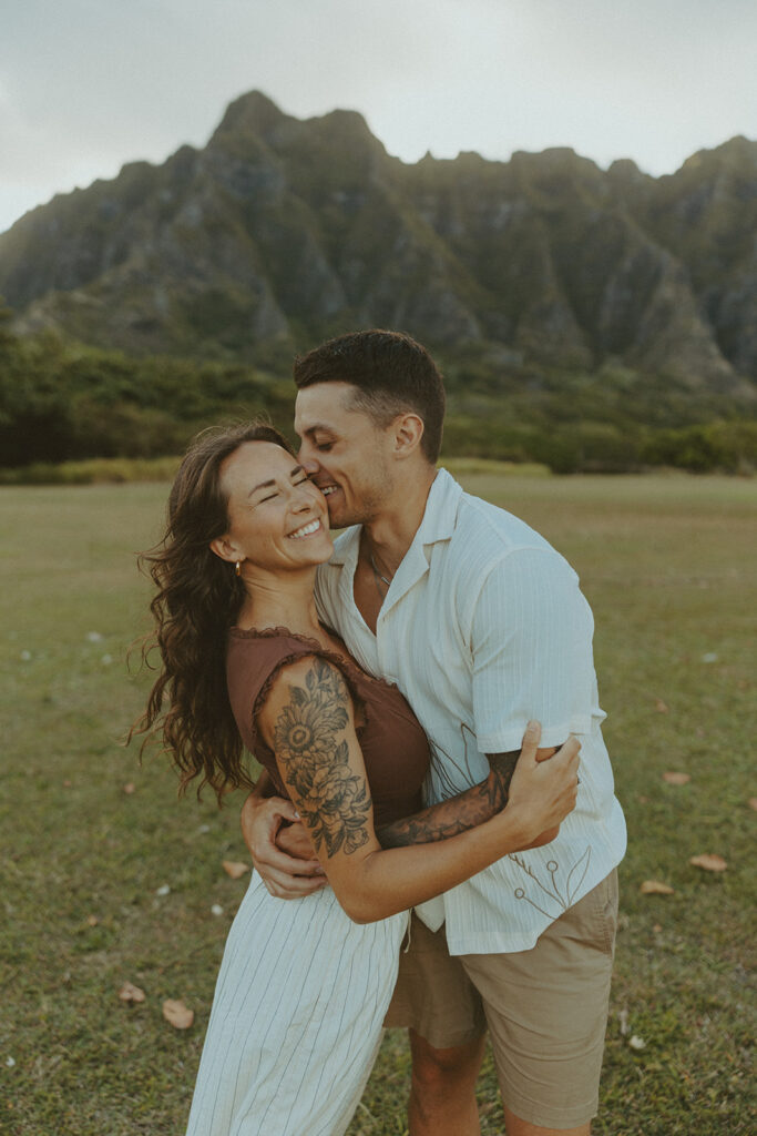 Couple walking along the shoreline at Kualoa Regional Park with ocean and mountain views in the background
