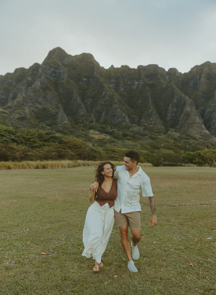 Couple walking along the shoreline at Kualoa Regional Park with ocean and mountain views in the background
