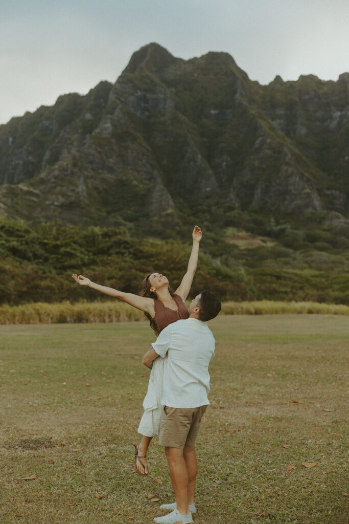 Couple walking along the shoreline at Kualoa Regional Park with ocean and mountain views in the background
