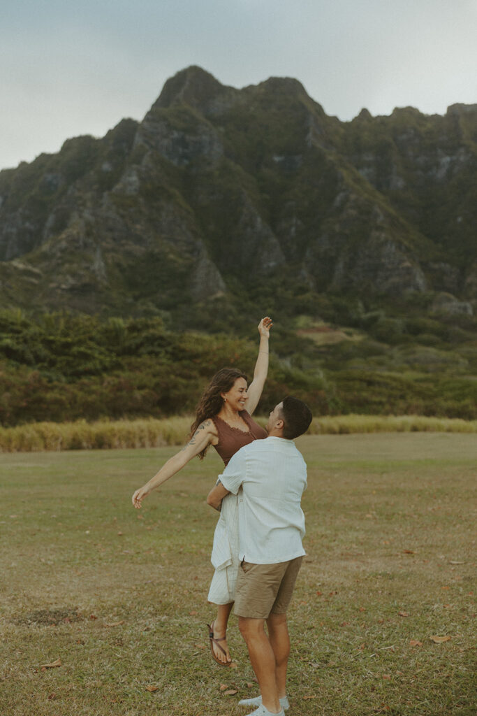 Couple walking along the shoreline at Kualoa Regional Park with ocean and mountain views in the background
