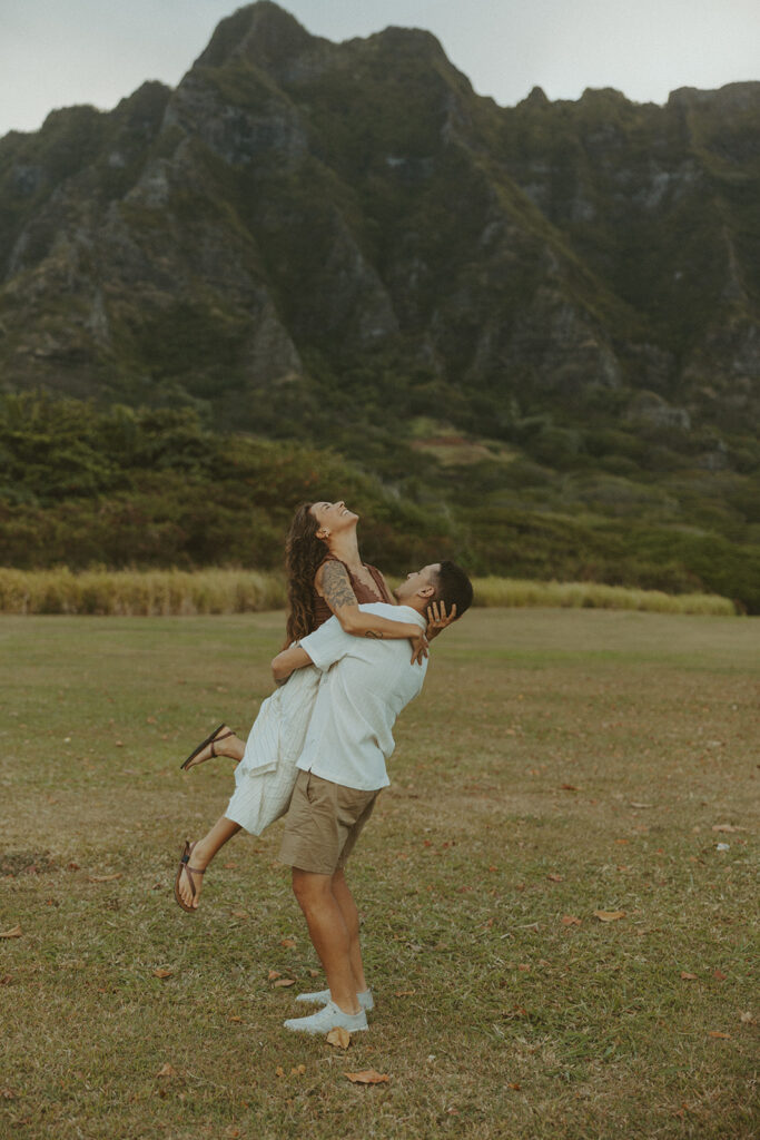 Couple walking along the shoreline at Kualoa Regional Park with ocean and mountain views in the background
