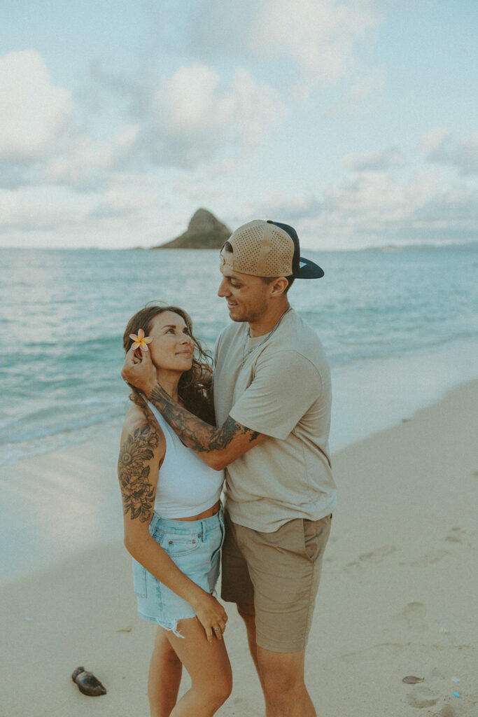 Couple walking along the shoreline at Kualoa Regional Park with ocean and mountain views in the background
