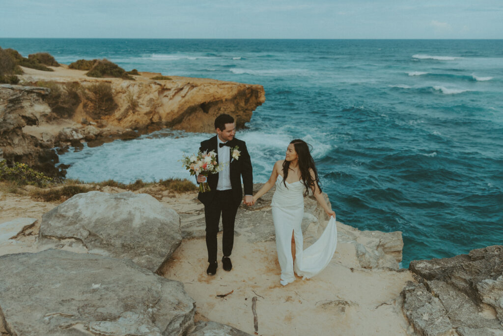 Newlyweds walking hand in hand along the cliffs at Shipwreck Beach during their Kauai elopement
