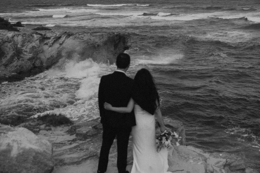 Newlyweds walking hand in hand along the cliffs at Shipwreck Beach during their Kauai elopement

