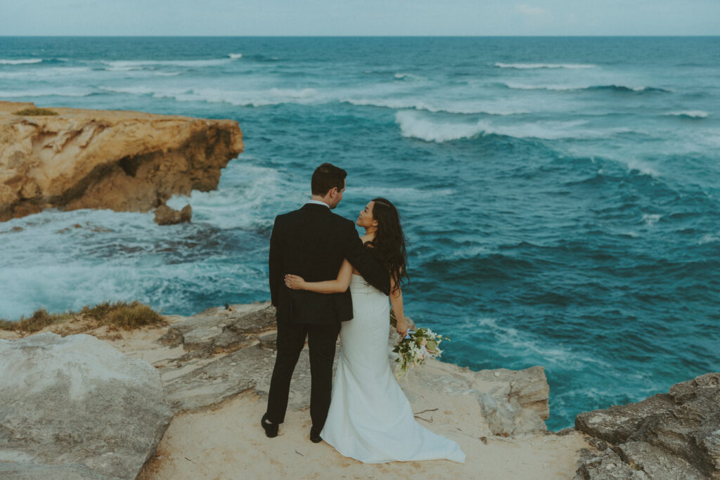 Newlyweds walking hand in hand along the cliffs at Shipwreck Beach during their Kauai elopement
