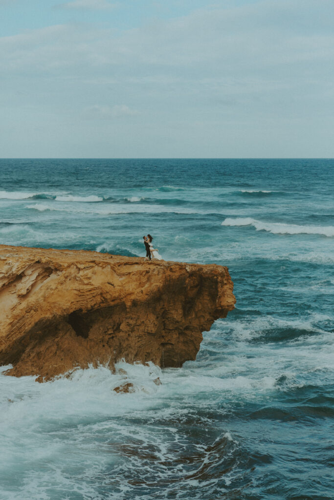 Newlyweds walking hand in hand along the cliffs at Shipwreck Beach during their Kauai elopement
