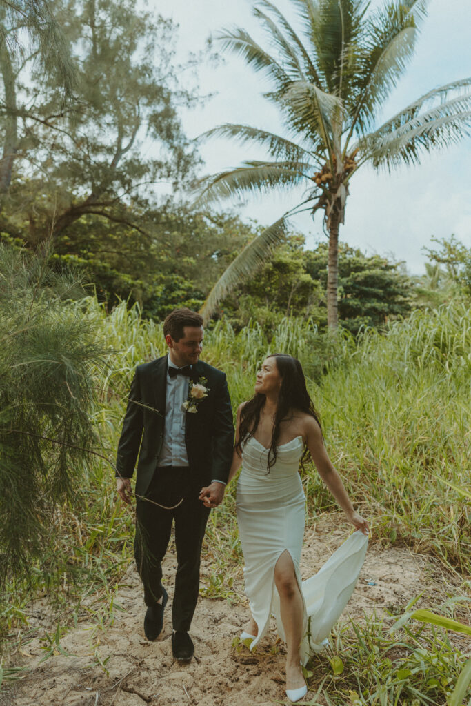 Bride and groom holding hands and smiling after their Shipwreck Beach elopement with ocean waves behind them
