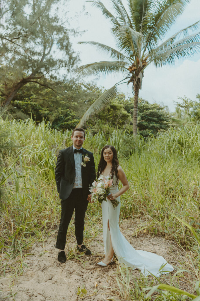 Bride and groom holding hands and smiling after their Shipwreck Beach elopement with ocean waves behind them