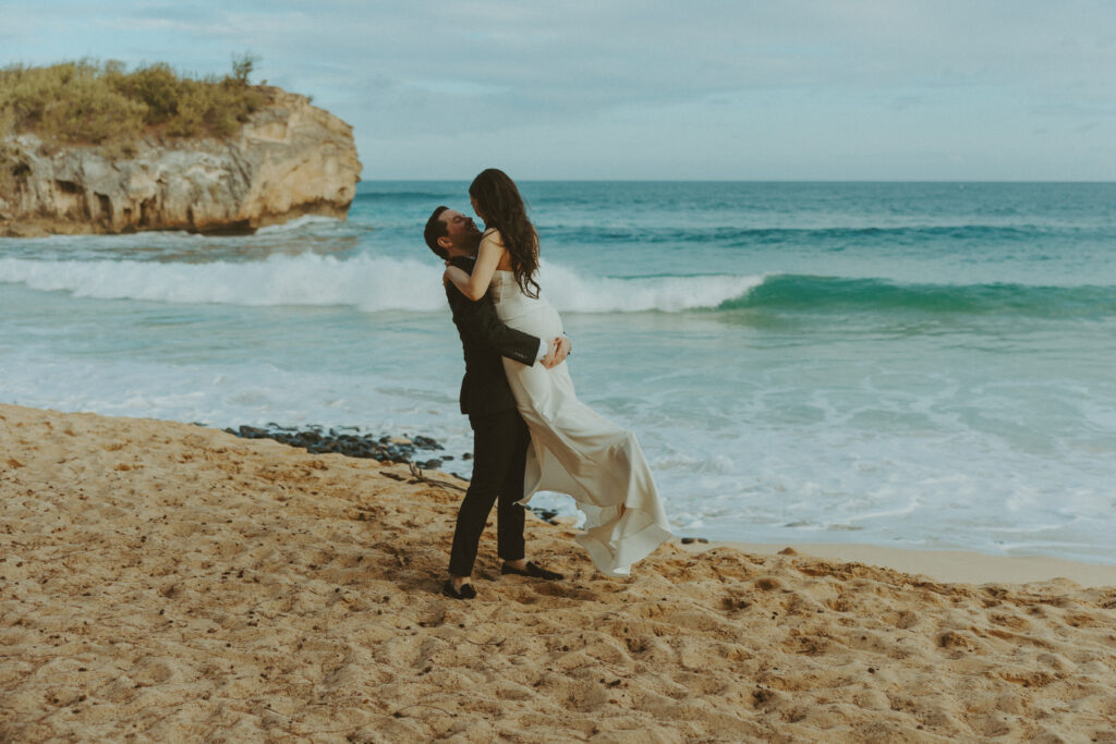 Bride and groom holding hands and smiling after their Shipwreck Beach elopement with ocean waves behind them
