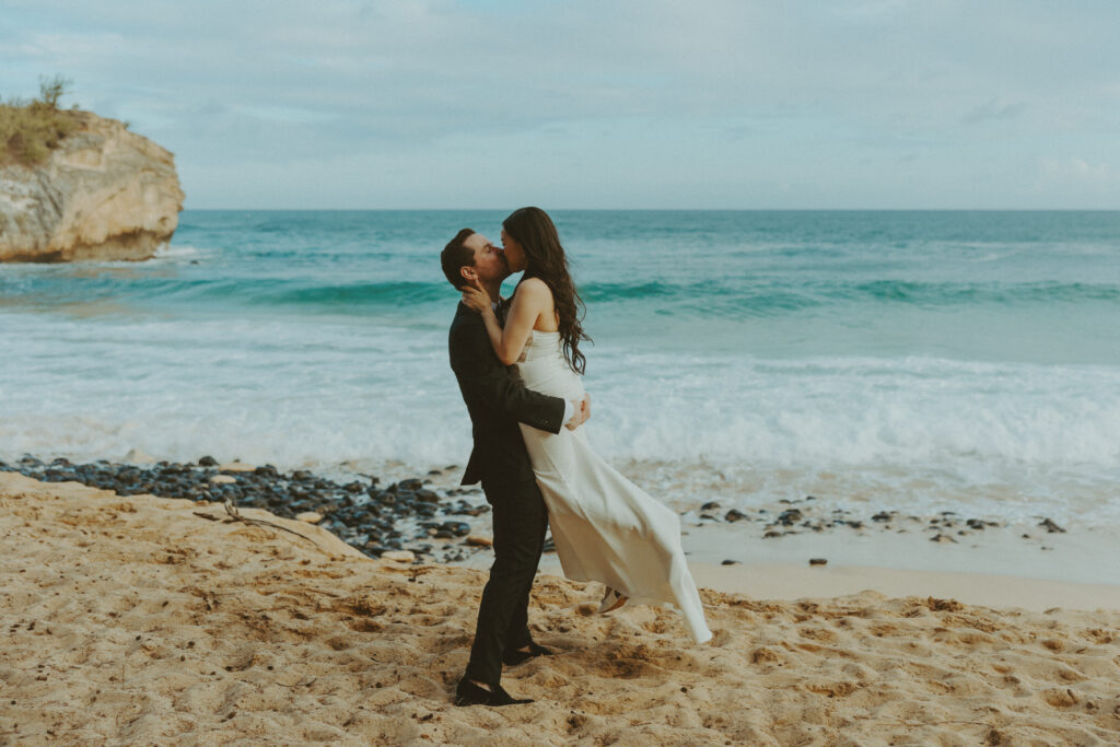 Bride and groom holding hands and smiling after their Shipwreck Beach elopement with ocean waves behind them
