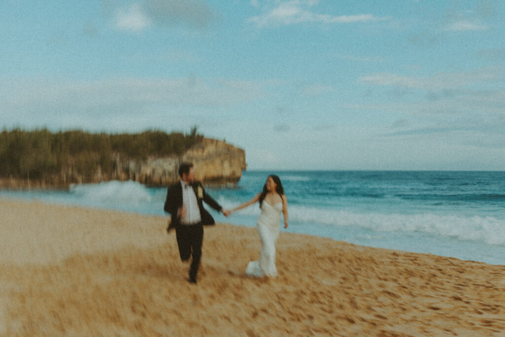 Bride and groom holding hands and smiling after their Shipwreck Beach elopement with ocean waves behind them
