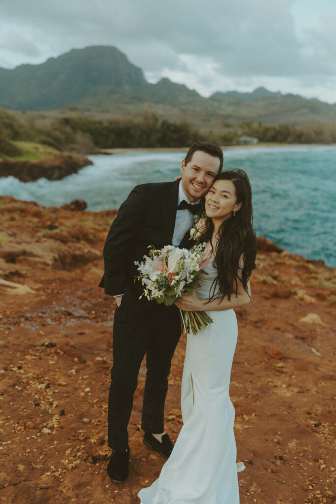 Bride and groom holding hands and smiling after their Shipwreck Beach elopement with ocean waves behind them
