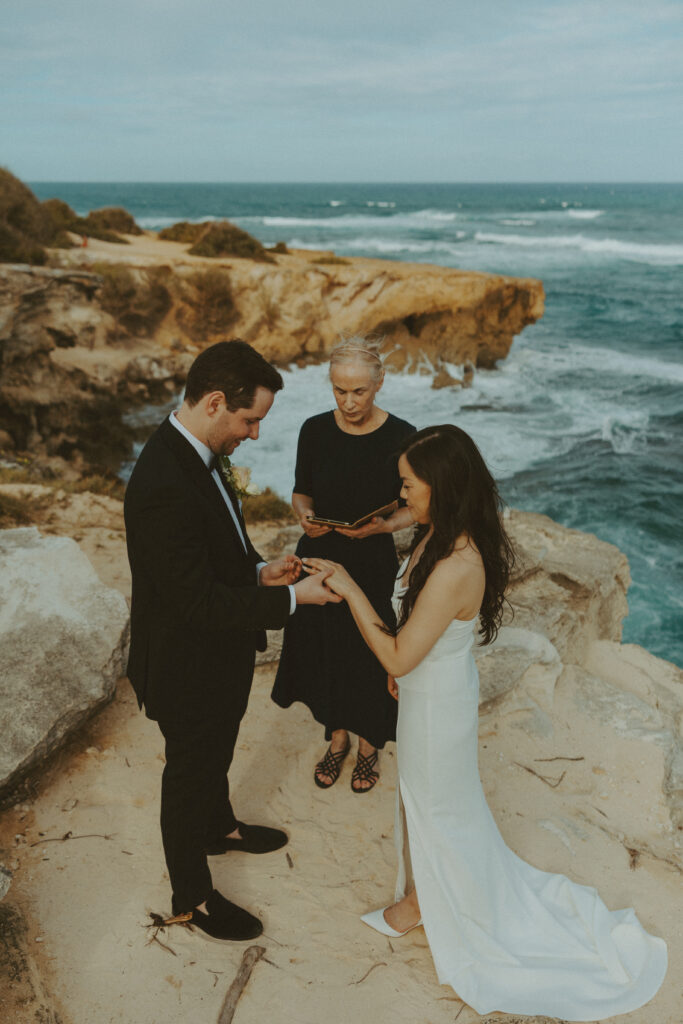 Bride and groom holding hands and smiling after their Shipwreck Beach elopement with ocean waves behind them
