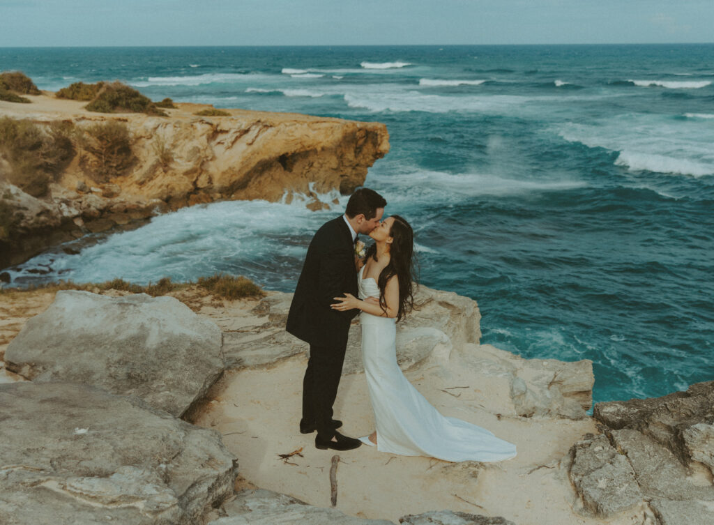 Bride and groom holding hands and smiling after their Shipwreck Beach elopement with ocean waves behind them
